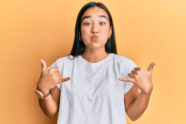 Genç Asyalı kadın, elleri şişmiş, komik yüzüyle shaka işareti yapıyor. Ağzı havayla şişer, havayı yakalar.. 