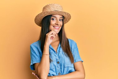 Yaz şapkası takan genç İspanyol kadın kameraya kollarını kavuşturmuş ve çenesi üzerinde kendinden emin bir şekilde bakıyor. Olumlu düşünmek. 