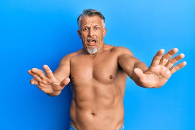 Orta yaşlı, gri saçlı, üstsüz ve korkudan dehşete düşmüş bir adam. El kol hareketi yapmayı kes, şok içinde bağır. panik konsepti. 
