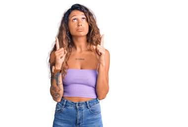 Dövmeli genç İspanyol bir kadın. Günlük giysiler giyiyor. Üzgün ve üzgün görünüyor. Parmaklarıyla yönü gösteriyor.. 