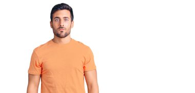 Yüzünde ciddi bir ifade olan günlük kıyafetler giyen genç bir İspanyol. Basit ve doğal bir şekilde kameraya bakıyorsun.. 