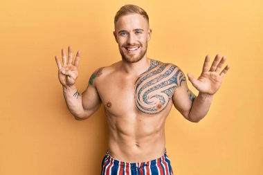 Mayo giyen genç, beyaz bir adam dokuz numarayı gösterip gülümserken kendinden emin ve mutlu görünüyor.. 