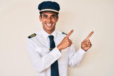 Uçak pilotu üniforması giyen genç İspanyol adam gülümsüyor ve kameraya bakıyor iki eliyle ve parmaklarıyla kenarı işaret ediyor.. 