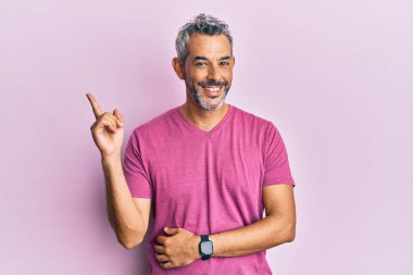 Orta yaşlı, gri saçlı, günlük kıyafetler giyen, gülümseyen, mutlu, eli ve parmağı yanda olan bir adam. 