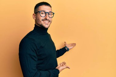 Balıkçı yaka kazak ve gözlük takan yakışıklı adam gülümseyerek doğal bir şekilde içeri girmeye davet ediyor. 