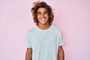 Yüzünde mutlu ve havalı bir gülümseme olan sıradan kıyafetler giyen genç İspanyol bir adam. şanslı kişi. 