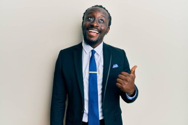 Yakışıklı, genç, siyah takım elbiseli, kravatlı, gülen yüzlü, başparmağıyla yüzünü gösteren bir adam.. 