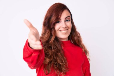 Genç ve güzel bir kadın günlük kıyafetler giyip gülümseyerek selamlaşma ve dostça el sıkışma sunuyor. başarılı iş. 