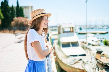 Genç sarışın kadın tatilde mutlu bir şekilde gülümsüyor. Kentin caddesinde korkuluklara yaslanıyor.