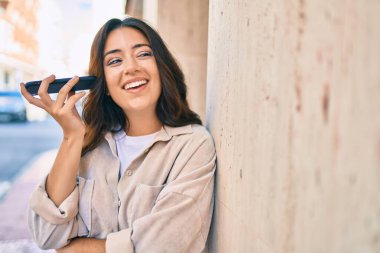 Genç İspanyol kadın gülümsüyor. Şehirdeki akıllı telefonu kullanarak mutlu bir sesli mesaj dinliyor..
