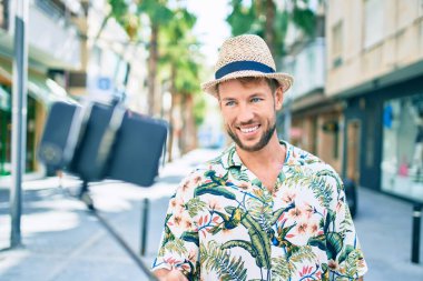 Beyaz tenli yakışıklı adam mutlu bir şekilde dışarıda selfie çekiyor. Selfie çubuğu kullanıyor.
