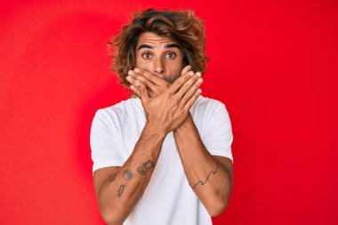 Gündelik beyaz tişört giyen genç İspanyol adam yanlışlıkla elleriyle ağzını kapatırken şok oldu. gizli kavram. 