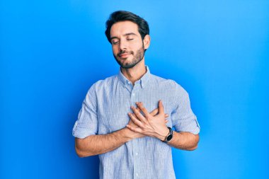 Zarif bir yaz gömleği giyen genç İspanyol adam elleri göğsünde, gözleri kapalı gülümsüyor ve yüzünde minnet ifadesi var. sağlık kavramı. 