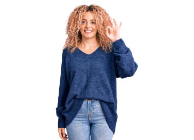 Kıvırcık saçlı, sıradan bir kazak giyen, gülümseyen, el ve parmaklarıyla 