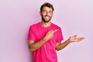 Pembe arka planda günlük pembe t-shirt giyen yakışıklı adam kameraya hayret ediyor ve gülümsüyor.. 