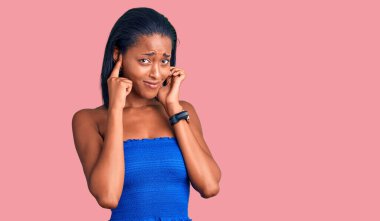 Genç Afro-Amerikan kadın, gündelik yaz kıyafetleri giyip yüksek sesli müzik sesi için kulaklarını parmaklarıyla kapatıyor. sağır kavramı. 