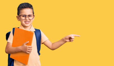 Okul çantası takmış, elinde kitapla gülümseyen küçük şirin bir çocuk. 