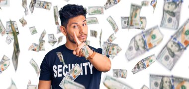 Güvenlik tişörtü giymiş yakışıklı Latin Amerikalı genç adam parmağını kaldırmış ve kızgın bir ifadeyle işaret ediyor.