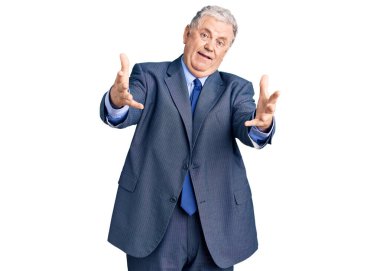 İş ceketi giyen yaşlı gri saçlı adam kameraya sarılıp kollarını açmış gülümsüyor. Mutluluğu kucaklayan neşeli bir ifade.. 