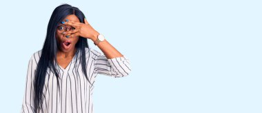 Genç Afro-Amerikalı kadın günlük kıyafetler ve gözlük takıyor. Şok olmuş bir şekilde yüzünü ve gözlerini kapatıyor. Utanmış bir ifadeyle parmaklarından bakıyor.. 