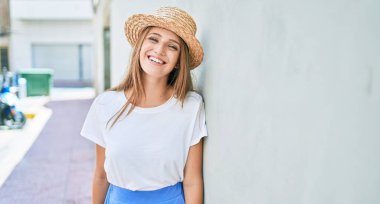 Genç sarışın kadın tatilde gülümsüyor. Mutlu bir şekilde şehrin duvarına yaslanıyor.