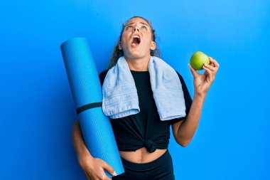 Güzel beyaz kız yoga minderi ve yeşil elma tutuyor kızgın ve kızgın çığlık atıyor sinirli ve öfkeli, öfkeyle bağırıyor.. 