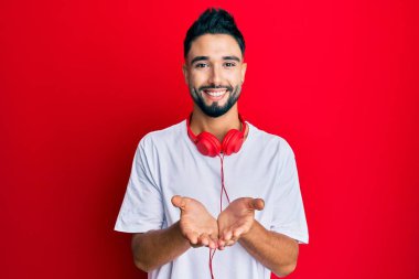Sakallı genç adam kulaklık kullanarak müzik dinliyor avuçlarıyla gülümsüyor ya da el hareketi yapıyor. Bekleme ve koruma 