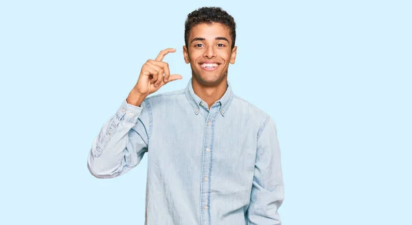 若いハンサムなアフリカ系アメリカ人の男性は カジュアルな服を着て笑顔と指を見て カメラで小さなサイズの看板を行う手で自信を持ってジェスチャー 概念を測定し — ストック写真