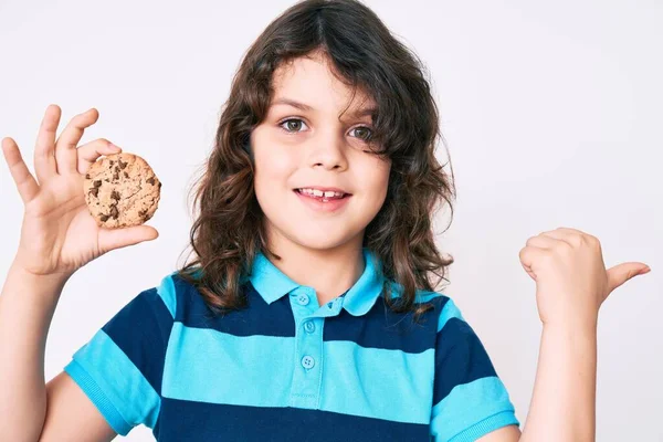 Cute Hispanic Child Long Hair Holding Cookie Pointing Thumb Side — Stock Photo, Image