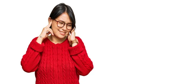 短い髪の若い美しいヒスパニック系の女性は 大きな音楽のノイズのためのいらいらした表情で指で耳をカバーカジュアルなセーターや眼鏡を着ています 聴覚障害の概念 — ストック写真