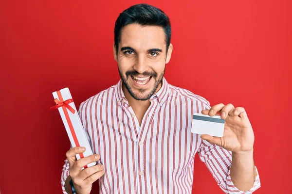 Νεαρός Ισπανόφωνος Κρατώντας Δώρο Και Πιστωτική Κάρτα Χαμογελώντας Και Γελώντας — Φωτογραφία Αρχείου