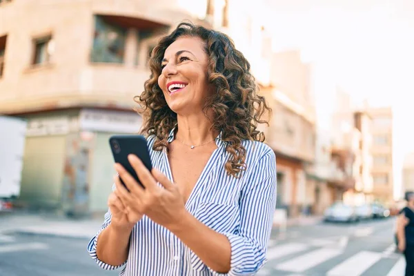 Middle age hispanic woman smiling happy and using smartphone at the city.