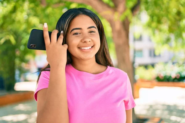 Young latin woman smiling happy listening audio message using smartphone at the park.