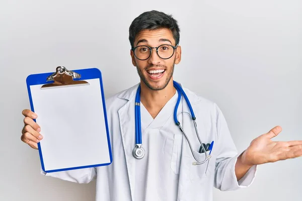 Jovem Homem Bonito Vestindo Estetoscópio Médico Segurando Prancheta Celebrando Realização — Fotografia de Stock