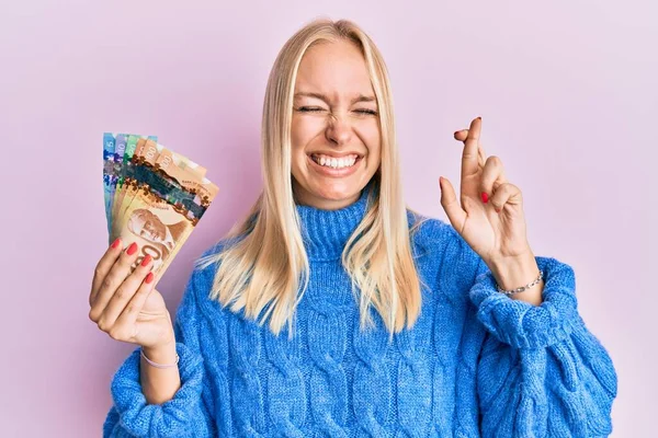 Young Blonde Girl Holding Canadian Dollars Gesturing Finger Crossed Smiling — Stock Photo, Image