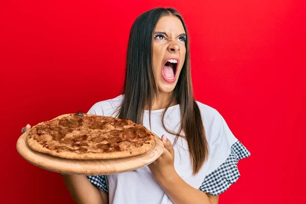 Young Hispanic Woman Holding Italian Pizza Angry Mad Screaming Frustrated — 图库照片