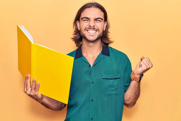 Joven Hombre Guapo Sosteniendo Libro Gritando Orgulloso Celebrando Victoria Éxito —  Fotos de Stock