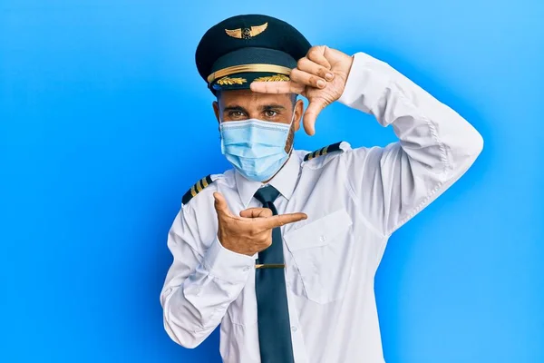髭を生やしたハンサムな男は 飛行機のパイロットの制服を着て安全マスク笑顔の顔を持つ手と指でフレームを作ります 創造性と写真の概念 — ストック写真