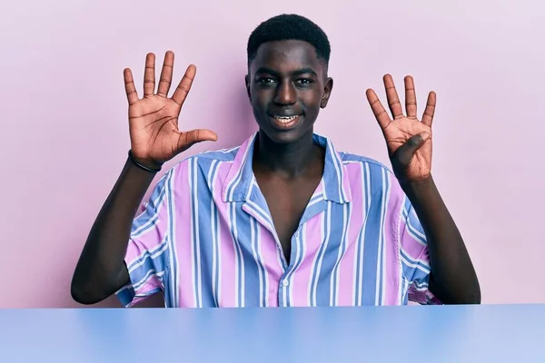 身穿休闲装的年轻的非洲裔美国人坐在桌子上 用9号手指指着桌子 面带微笑 自信而快乐 — 图库照片