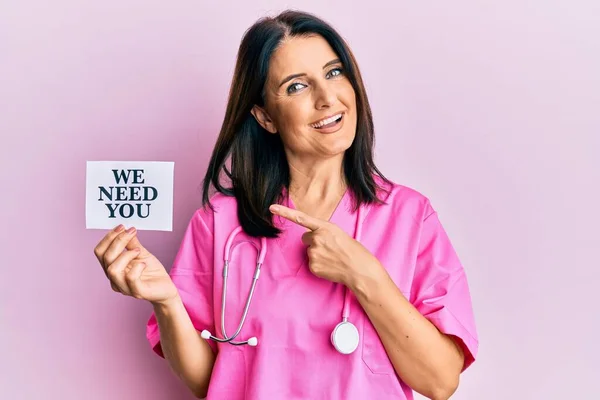 Middle age brunette doctor woman wearing doctor uniform and stethoscope smiling happy pointing with hand and finger