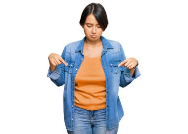 Genç, kısa saçlı, sıradan kot ceketli, üzgün ve üzgün görünen, yönünü parmaklarıyla belirten, mutsuz ve depresif bir kadın.. 