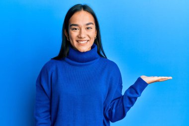 Genç Asyalı kadın, günlük kışlık süveter giyip neşeli bir şekilde sunum yapıyor ve avuç içi kameraya bakıyor.. 