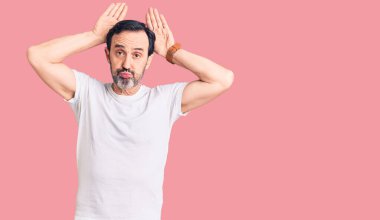 Orta yaşlı, tişört giyen, tavşan kulağı hareketi yapan, elleri avuçlarında, alaycı ve şüpheci görünen yakışıklı bir adam. Paskalya tavşanı konsepti. 