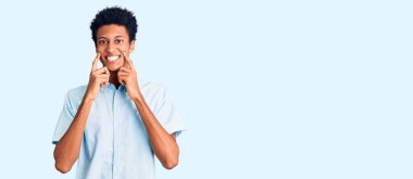 Genç Afro-Amerikalı, günlük kıyafetler giymiş ağzı açık gülümseyen, parmakları işaret eden ve neşeli gülümsemeye zorlayan bir adam. 