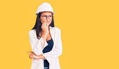 Mimar şapkası ve gözlük takan genç ve güzel bir Latin kız gergin ve elleri ağızda tırnak yerken gergin görünüyor. anksiyete. 