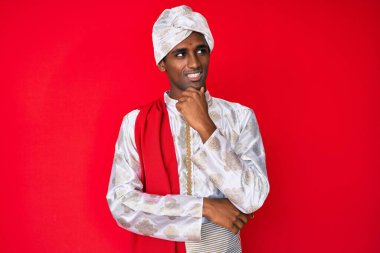 Sherwani sari giysileri giyen yakışıklı Hintli adam çenesi üstünde soru sorarken düşünceli bir ifade takınıyor. Düşünceli bir yüzle gülümsüyor. şüphe kavramı. 