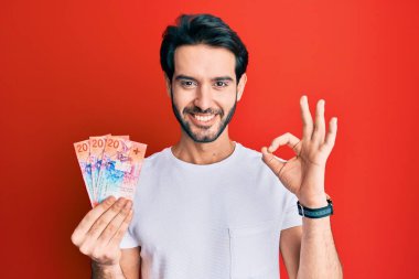 İspanyol asıllı genç adam İsviçre frangı banknotları tutuyor. Parmaklarıyla imza atıyor, gülümsüyor ve mükemmel bir sembol oluşturuyor. 