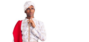 Gelenek giyinmiş Afrikalı yakışıklı bir adam Sherwani sari elbisesi giyiyor. Kuşkuya odaklanmış, çenesinde parmak olan ve kafasını kaldırıp merak eden biri. 