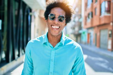 Genç, yakışıklı, Afro-Amerikan bir adam. Günlük kıyafetler ve güneş gözlüğü takıyor. Mutlu gülümsüyor. Yüzünde gülümsemeyle kasaba caddesinde yürürken.