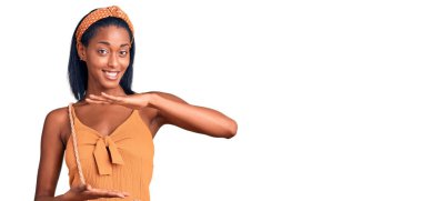 Genç Afrikalı Amerikalı kadın. Yazlık elbiseler giyiyordu. Elleri büyük ve büyük bir işaret, ölçü işareti gösteriyordu. Kameraya bakıp gülümsüyor. ölçüm kavramı. 